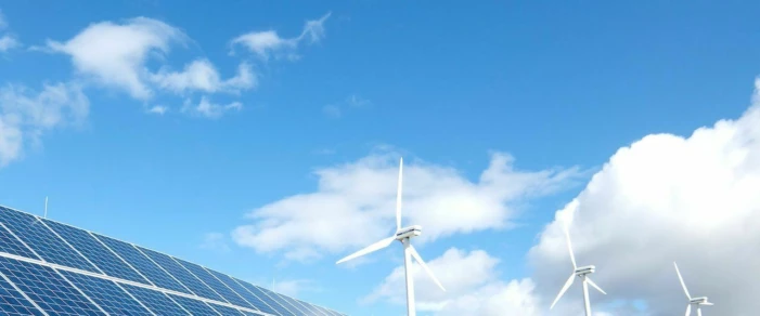 Solarzellen und sich drehende Windräder vor blauem Himmel mit vereinzelten Wolken.